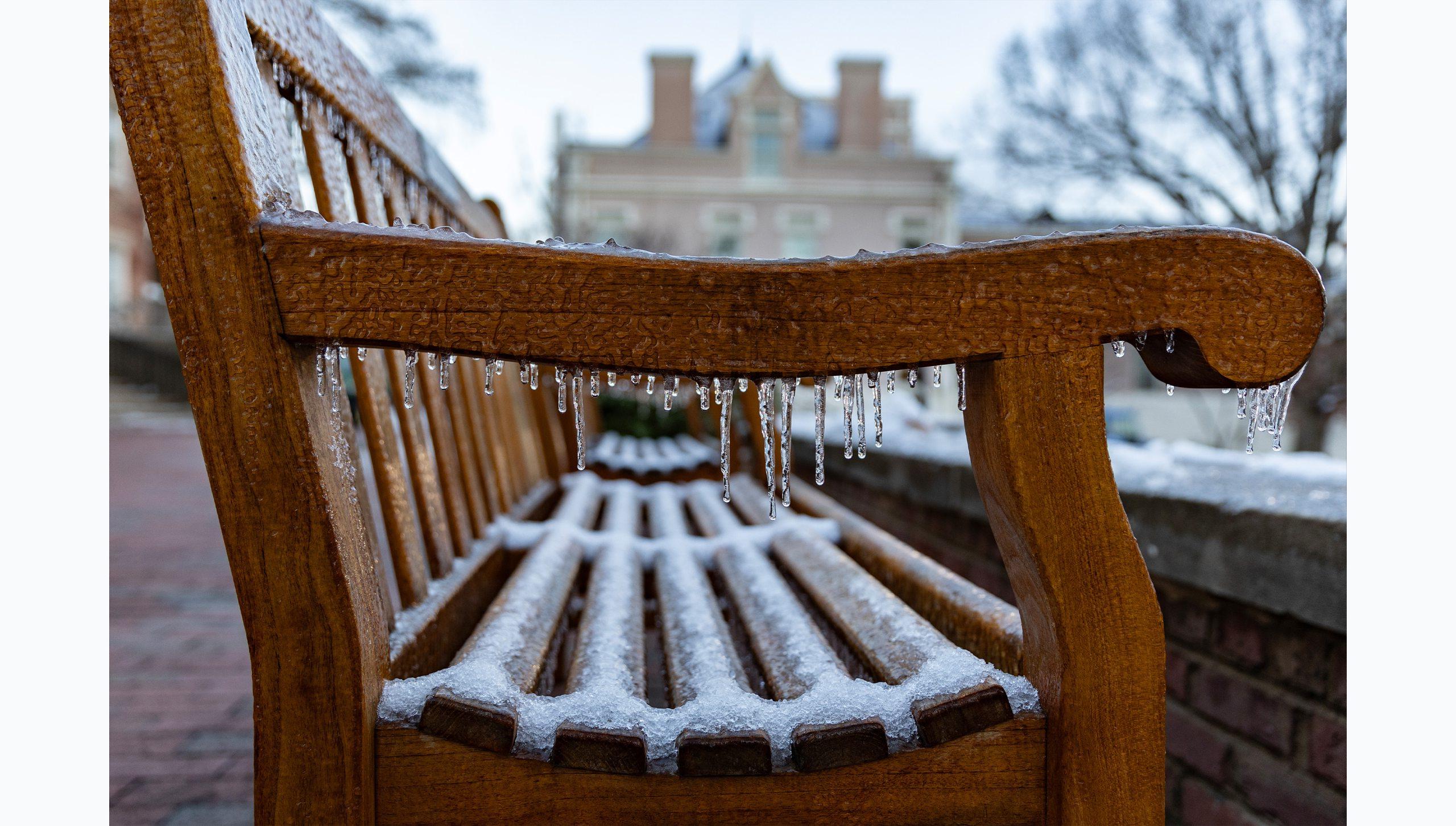 Close-up image of a wooden bench on the campus of U.N.C Chapel Hill covered with snow and icicles hanging of the side.